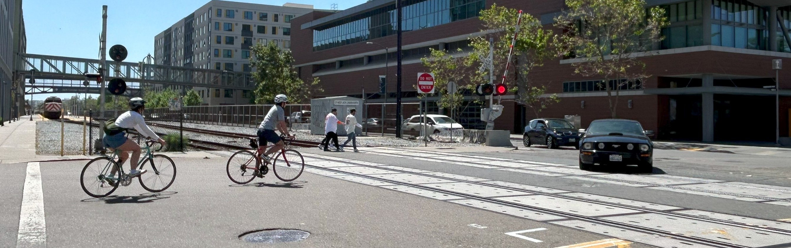 A photo showing pedestrians, bicyclists, and drivers crossing railroad tracks on Embarcadero West at Webster Street A photo showing pedestrians, bicyclists, and drivers crossing railroad tracks on Embarcadero West at Webster Street